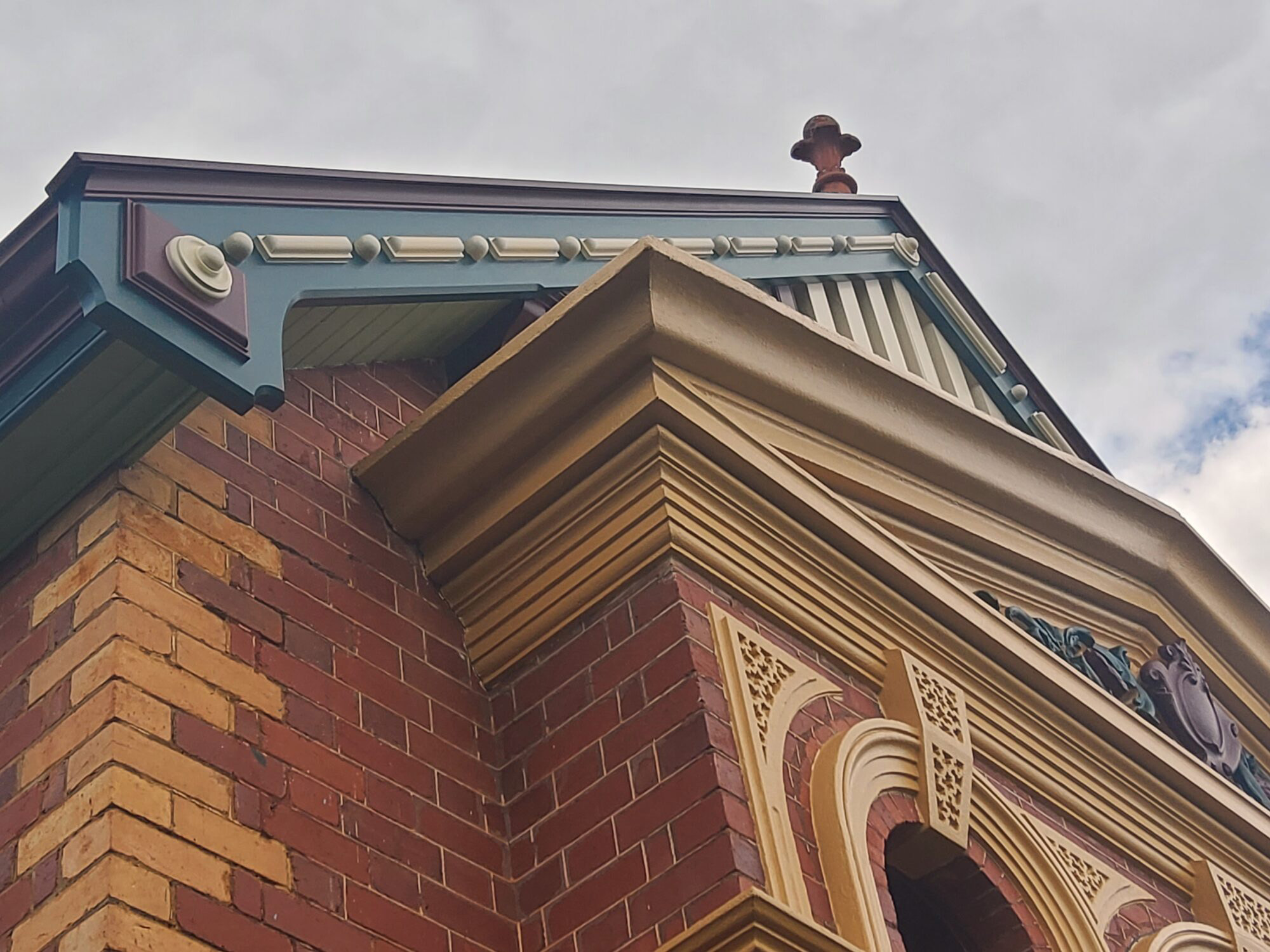 Looking up at the restored bargeboard, cornice and finial on a polychrome brick bay — Airlie