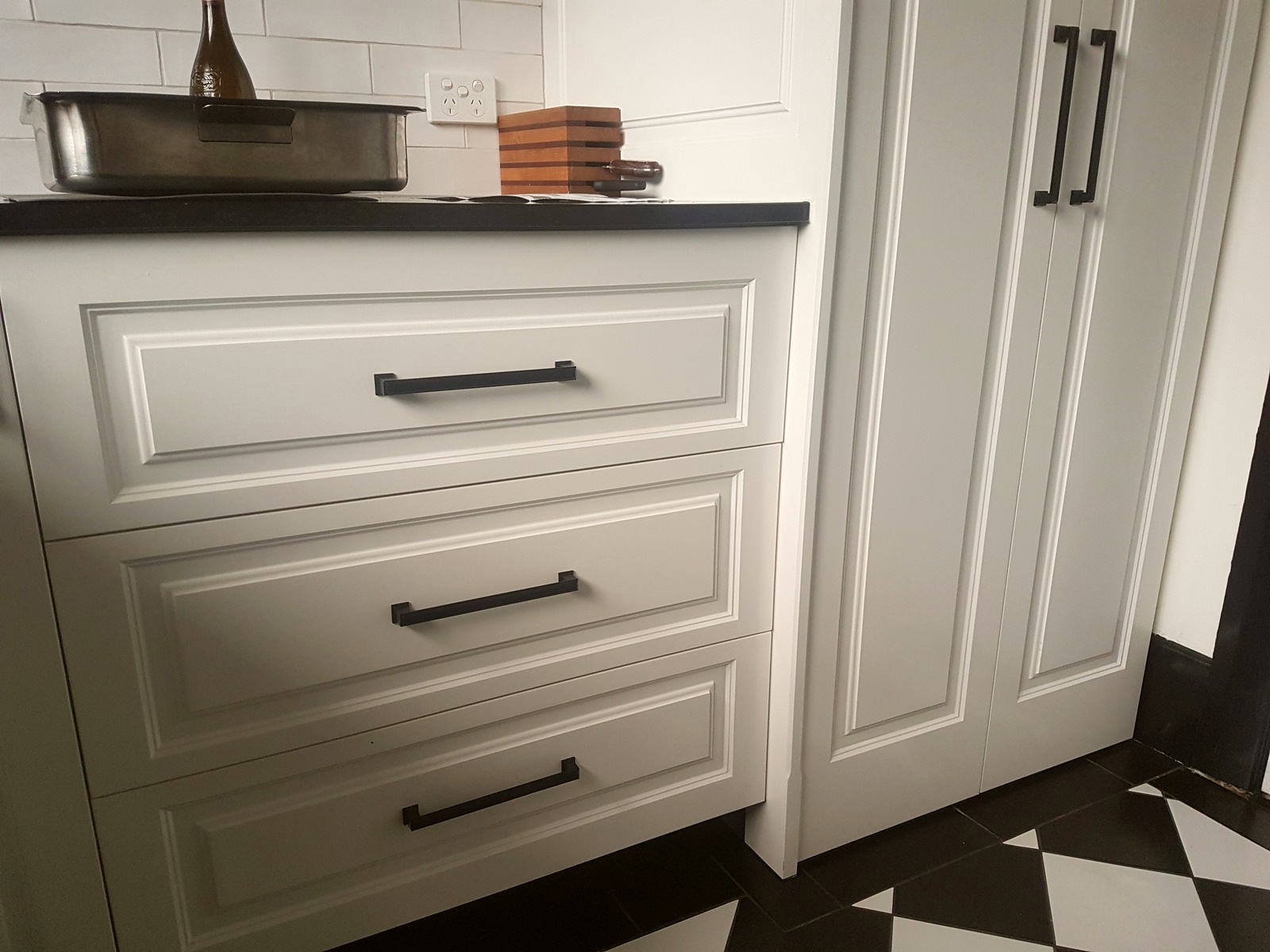 Art Deco kitchen cabinetry with raised panel doors and black hardware